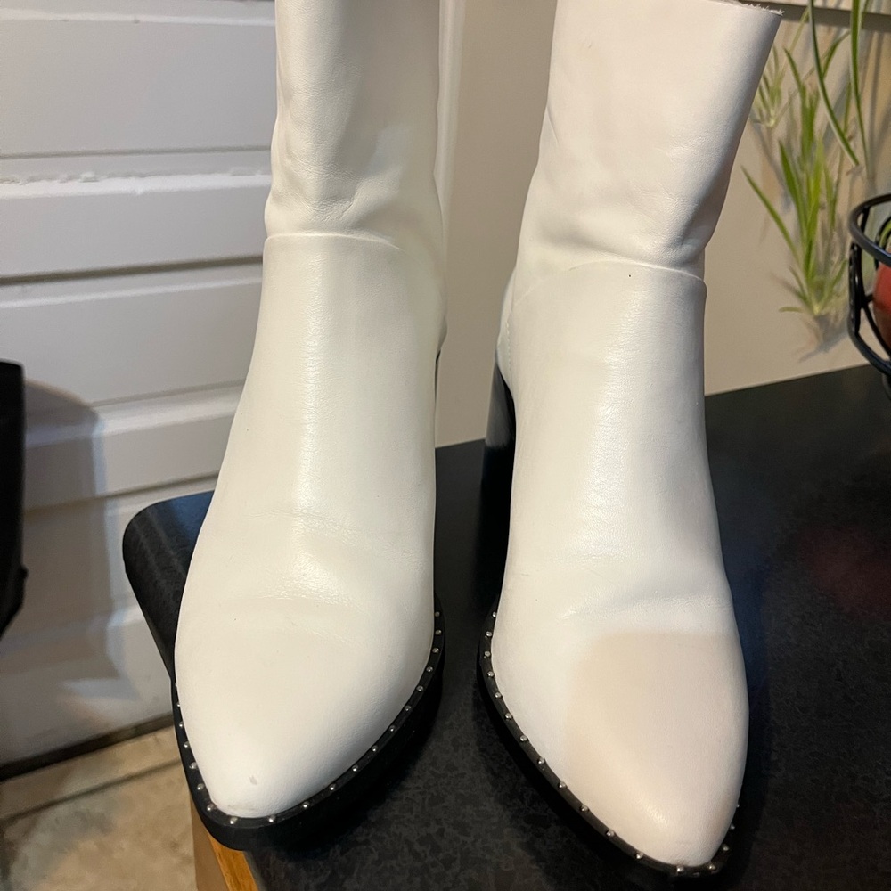 Women’s white leather booties with black block heel and stud trim.